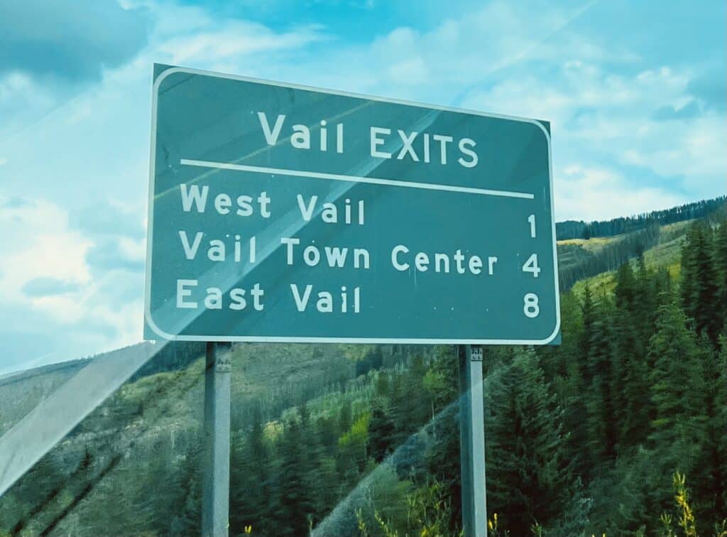 Road sign indicating distances to Vail exits: West Vail at 1 mile, Vail Town Center at 4 miles, and East Vail at 8 miles