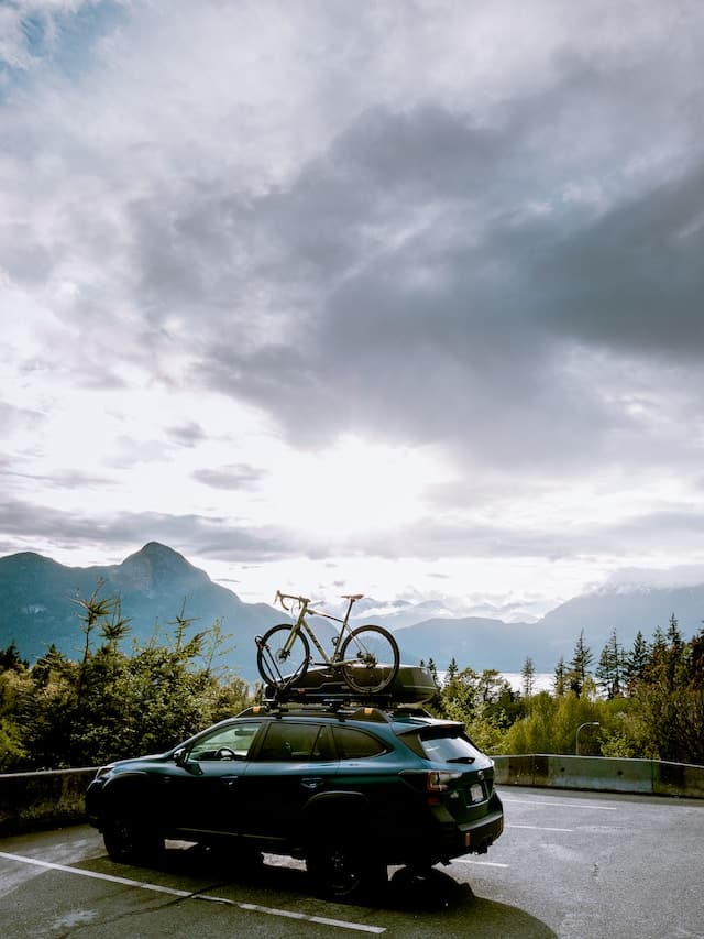 Subaru parked with its front facing a majestic mountain, equipped with a roof-mounted bike, ready for adventure.