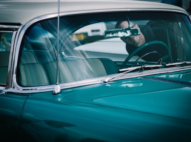 Man peering into the driver's seat window, admiring the interior of a vintage car.