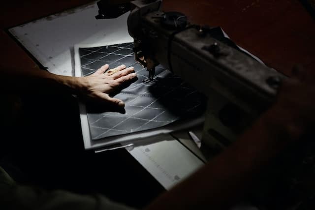 Close-up of a hand feeling the texture of fabric intended for car upholstery, with a sewing machine in the background