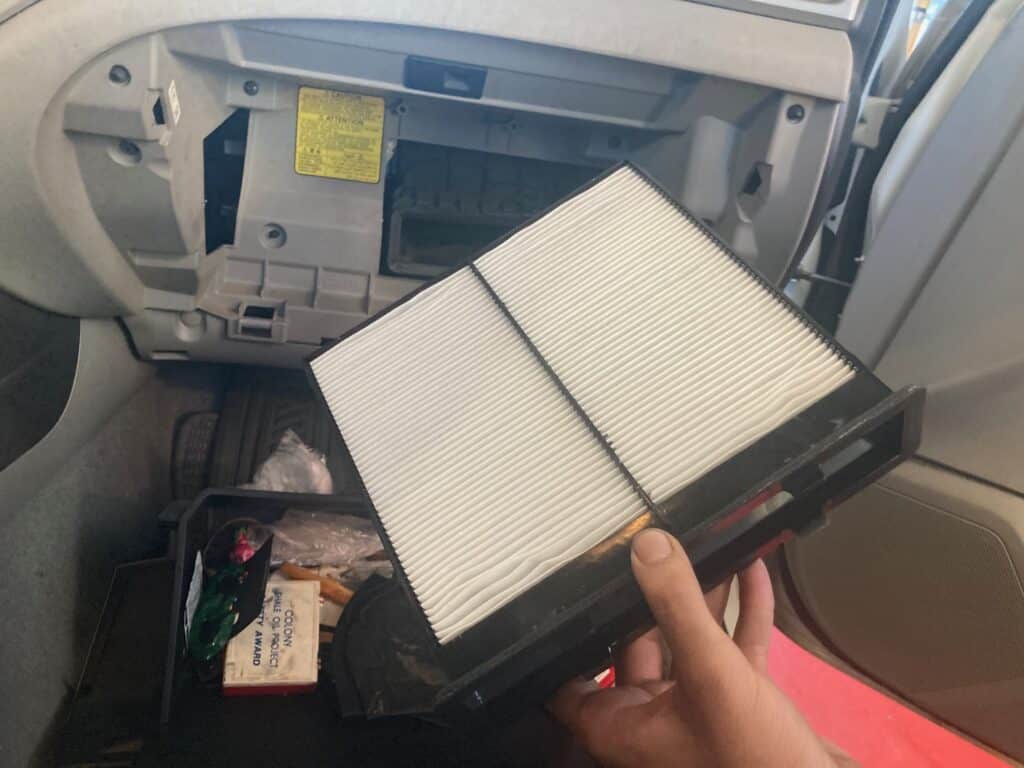 Hand displaying a pristine cabin air filter, poised for installation behind the vehicle's glove box.