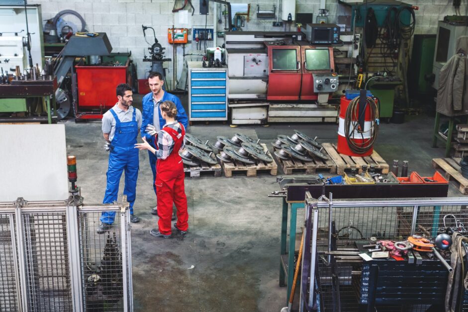 A photo illustrating three mechanics engaged in a discussion over a car experiencing jerking issues. The mechanics are shown examining the engine, with one pointing out specific components, indicating the multifaceted nature of diagnosing the problem. The image captures their serious expressions and focused attention, reflecting the complexity and multiple causality of car jerking issues. Tools and diagnostic equipment are visible in the background, highlighting the technical and professional approach required to address such problems.