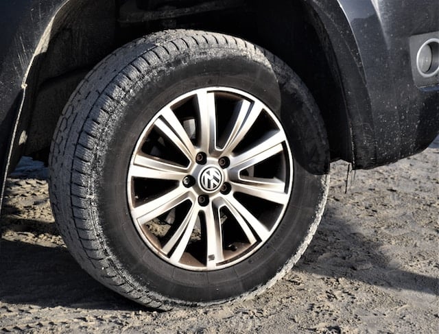 Close-up image of a car's wheel and fender, coated with dirt and sand, illustrating the fender's role in protecting the vehicle from road debris.